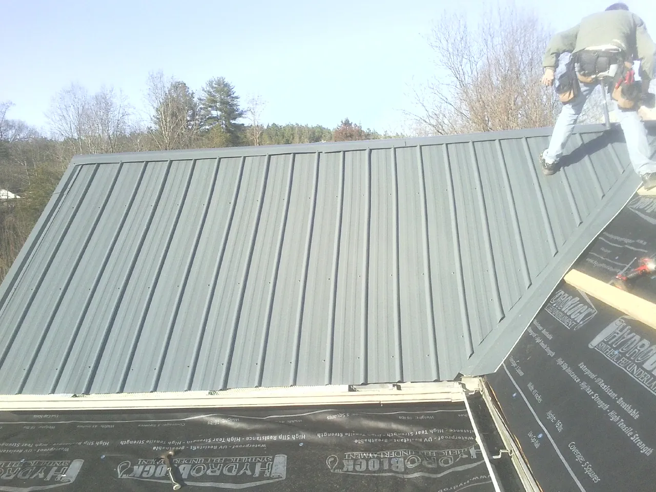 Crew installing dark green standing seam panels over synthetic underlayment in Swayzee