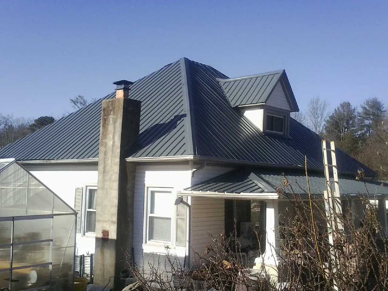 Dark blue standing seam metal roof on a white farmhouse with dormer — Slate & Tile Roof Repair by Roofing Brothers in Swayzee