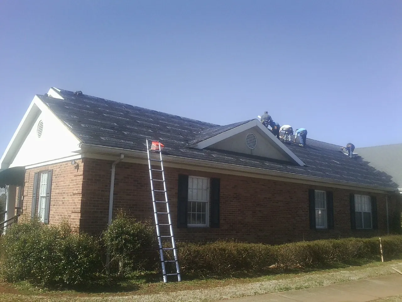 Crew tearing shingles off a brick ranch roof with a ladder set — Emergency Roof Repair work by our crew in Swayzee