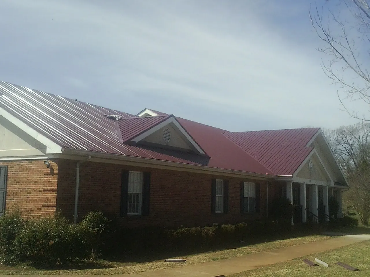 Red metal roof with gabled entries on a long brick building, from a Hail Damage Roof Repair job in Swayzee