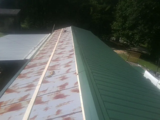 Old rusted panels beside newly installed green metal roofing — Wind Damage Roof Repair by Roofing Brothers in Swayzee