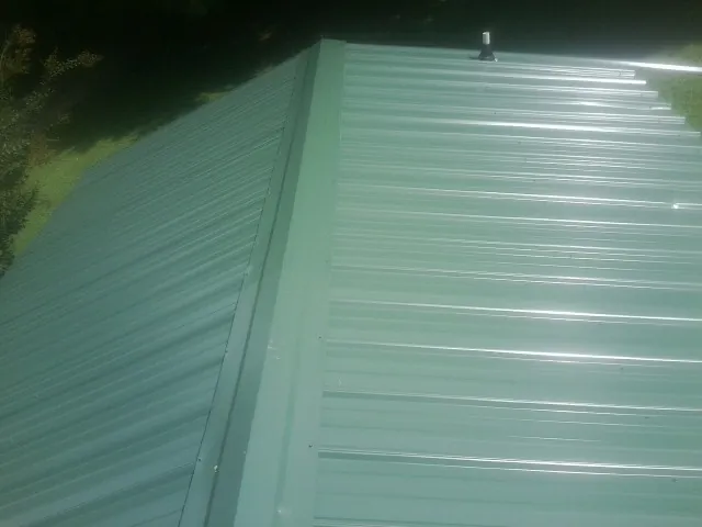 New green metal panels meeting at the ridge of a roof — Flat Roof Repair work by our crew in Swayzee