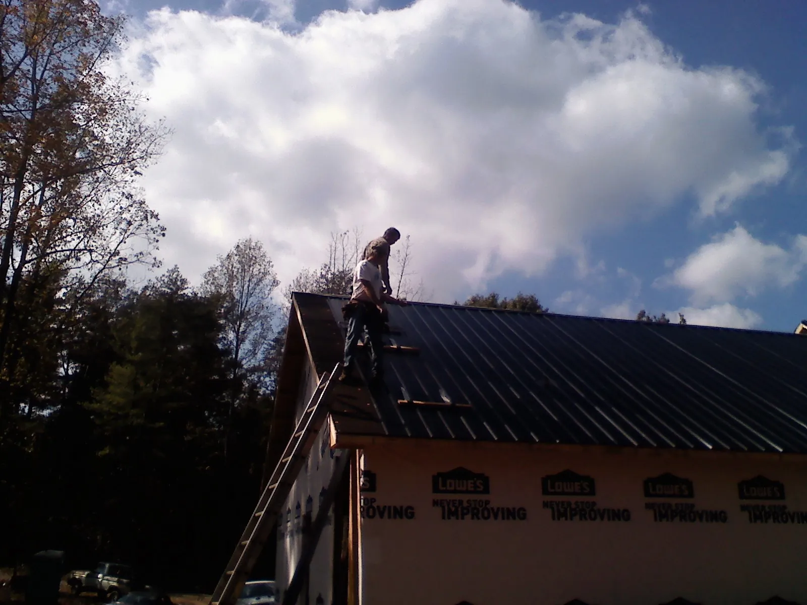 Roofer fastening dark metal panels high against a cloudy sky, from a Roof Inspection job in Swayzee