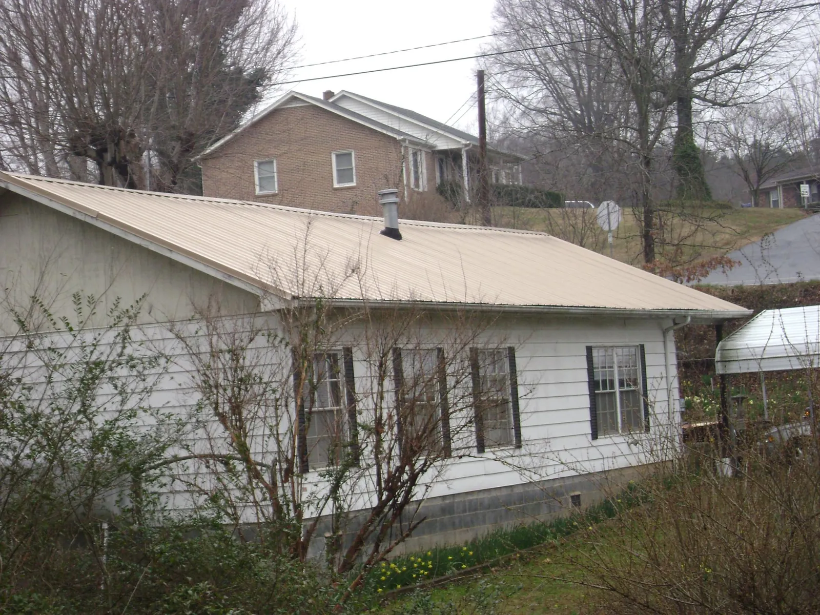 Tan metal roof on a white sided house set into a hillside — Commercial Roofing by Roofing Brothers in Swayzee