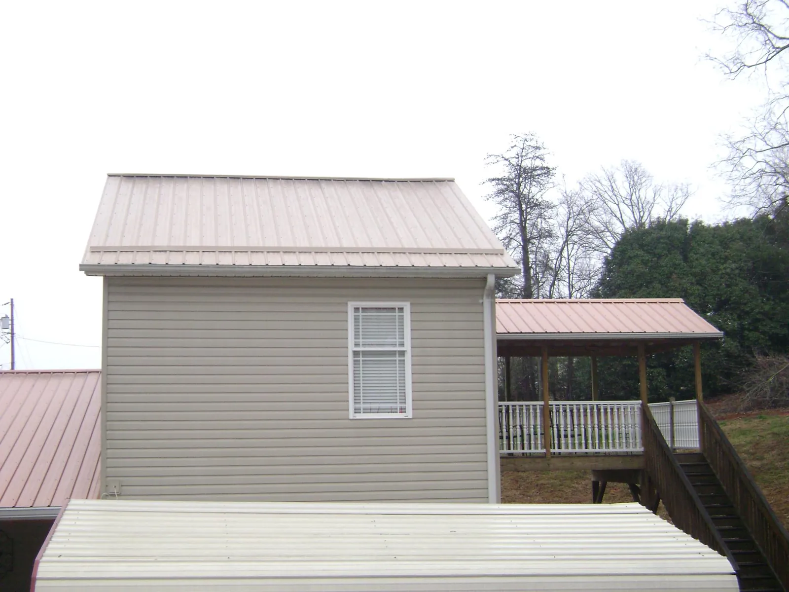 Tan metal roofs on a two story addition and attached porch, from a Roof Replacement job in Swayzee